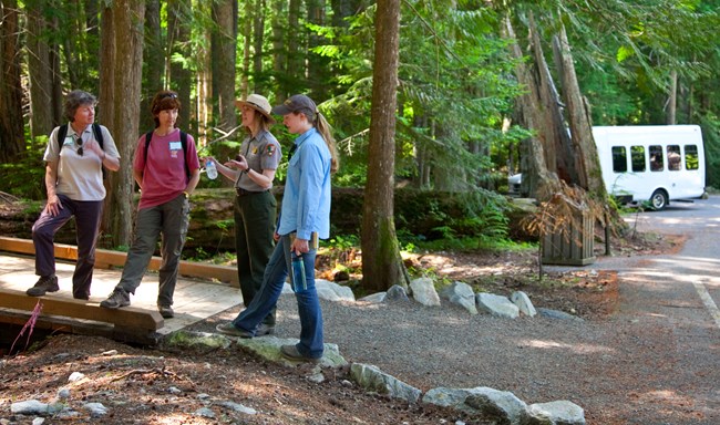 A ranger stands in the woods with visitors and shares information with them.