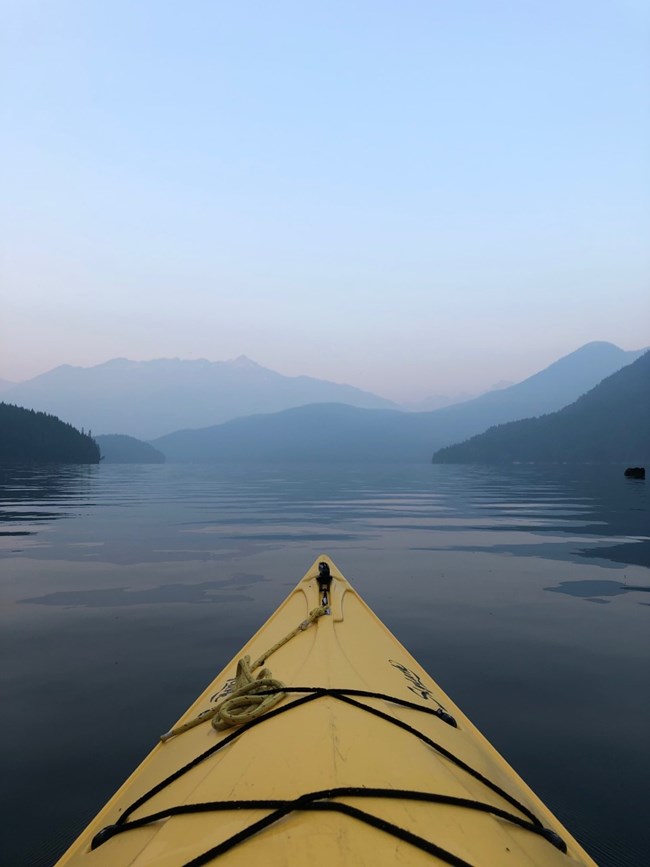 kayak on still mountain lake with distant peaks obscured by smoke
