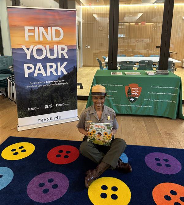 A park ranger sits cross-legged on the floor of a school.