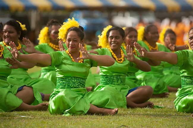 Young Samoan ladies perform while sitting and in traditional clothing.