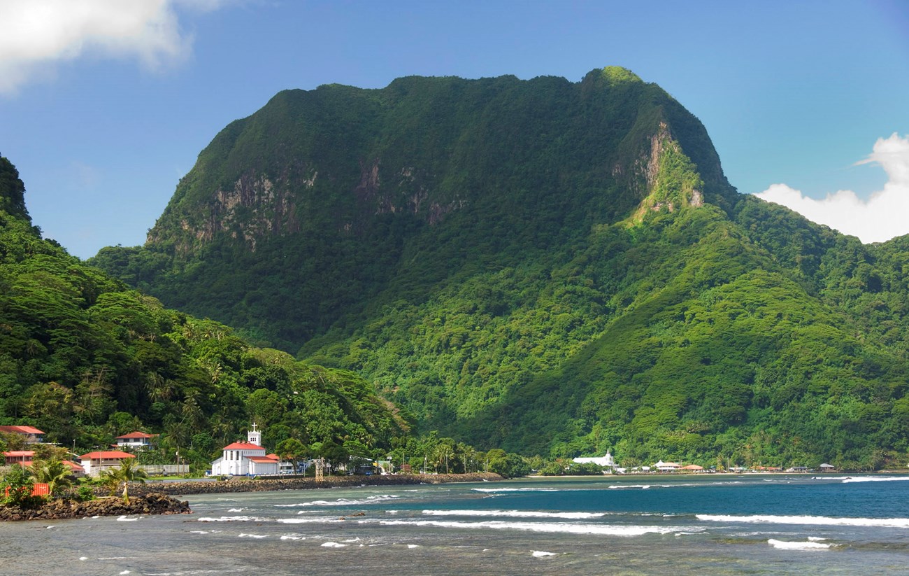 A scenic view of the ocean up against the beach and jutting mountains. Village in sight.