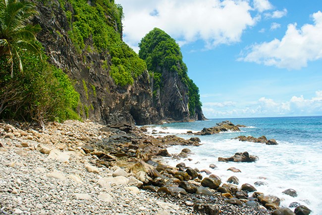 A rocky beach with beautiful mossy rock formations jutting up from the shore. The ocean waves lap against the short.