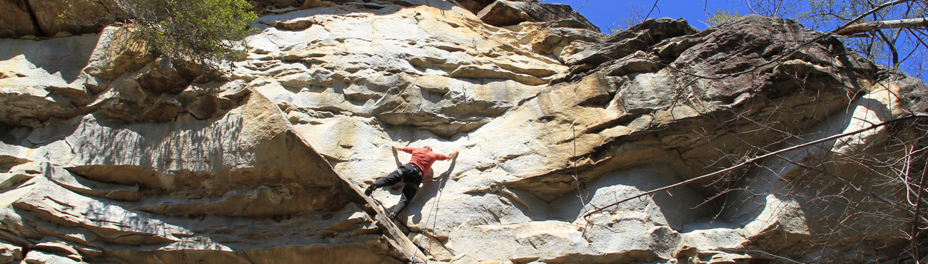 A rock climber scaling a rocky brown surfaced cliff.