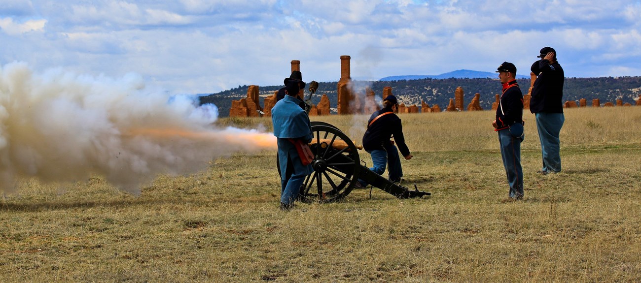 Staff fire a cannon with Fort  Union ruins in the distance.