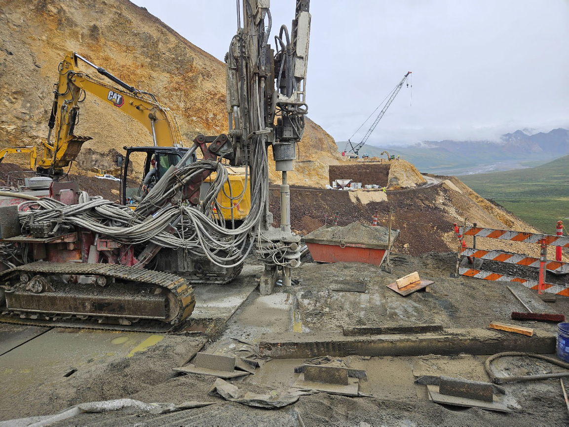 A drill rig positioned atop a cementous abutment drilling into the rock