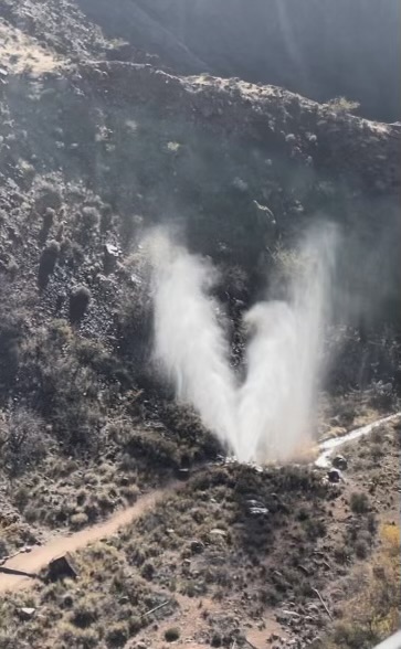 An aerial view of a pipeline spewing water approximately 50 feet high along a trail in the inner canyon