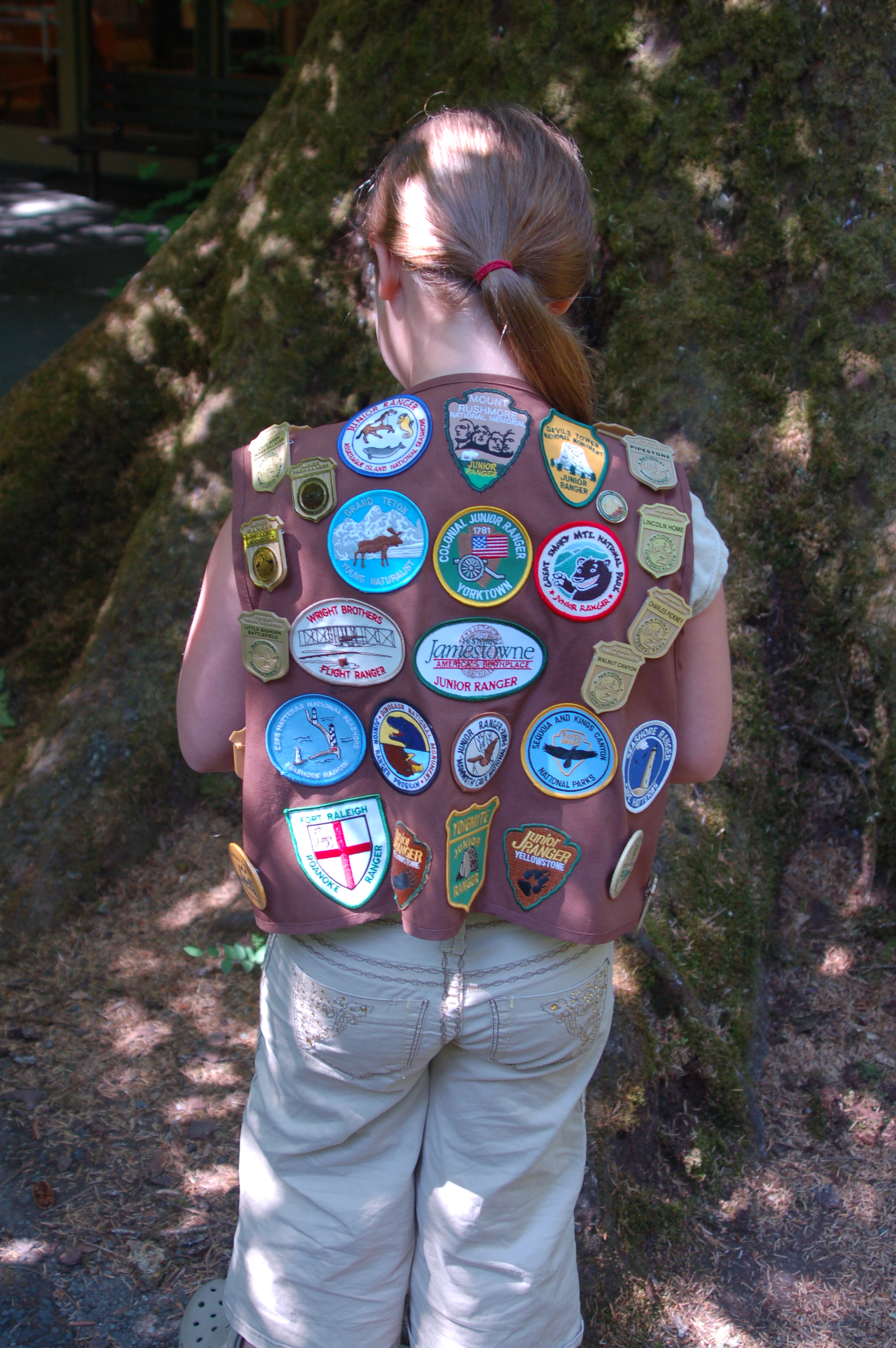 A young girl with a ponytail turned to show many junior ranger badges on the back of her vest.