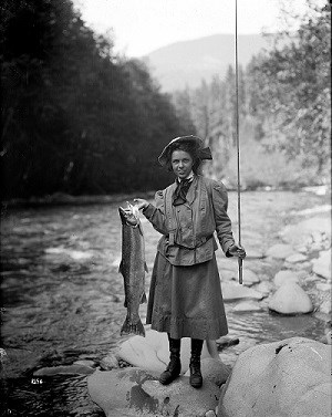 Historic image of a woman holding a large salmon near a river.