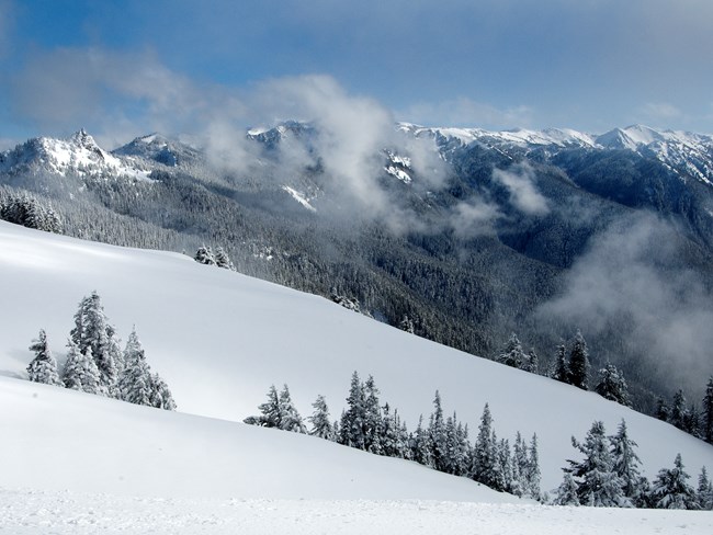 Clouds in front of a snow-covered mountain range.