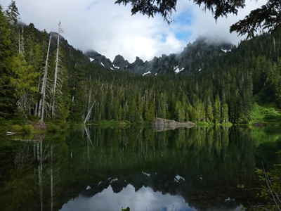 A lake with densely forested shores and a sharp mountain ridge above.