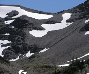 A large, steep rocky slope with multiple lingering snowfields. The rock structure types on the slope vary from loose scree to consolidated basaltic rock.
