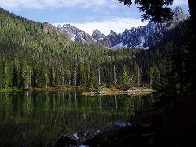A lake with densely forested shores and a sharp mountain ridge above.