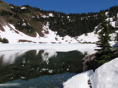 Hoh Lake, partially covered in ice with snowfields bordering its shores.