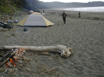 A small fire near a tent on the beach.