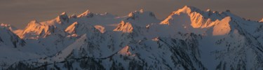 The alpenglow of sunset lights the snow-capped peaks of a mountain range.
