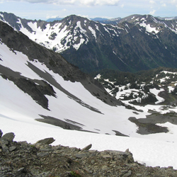 A mountain view as seen from Cameron Pass. A snowy basin lies below, and a snowy mountain ridge rises in the background.