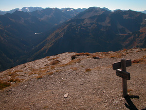 A vantage point from a high trail junction. A wooden trail sign sits in the foreground. A valley and mountains can be seen farther out. The sky has a slightly hazy look to it.