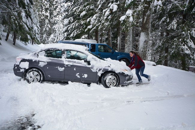 Oregon Caves staff member pushing car buried in snow.