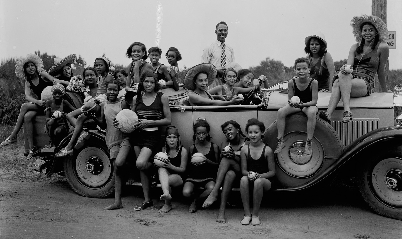 Twenty-two individuals pose for a photo sitting on or standing around a vehicle. The image is in black and white and was taken in 1931 at a YMCA camp.