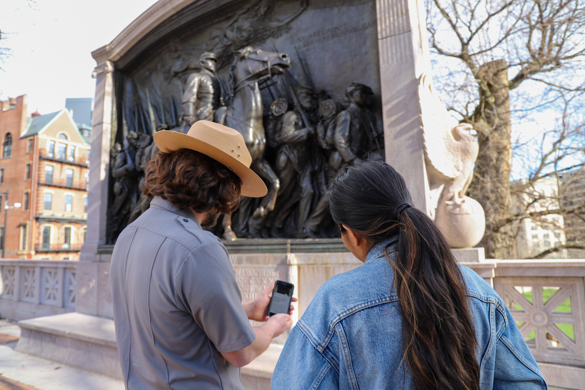A park ranger points at the NPS App on a visitor's cell phone while they stand in front of a monument dedicated to African American soldiers