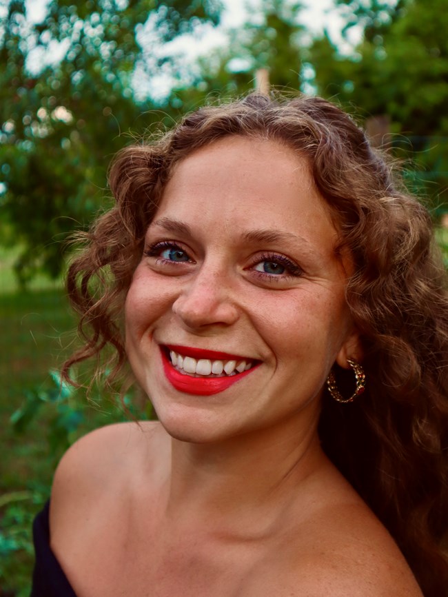 Headshot of a white woman with curly brown hair and a wide smile