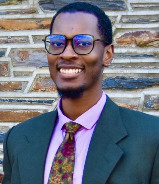 Headshot of a Black man wearing a green suit jacket, pink shirt and floral tie