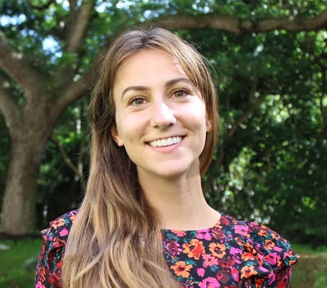 Headshot of a white woman with long brown hair wearing a floral dress