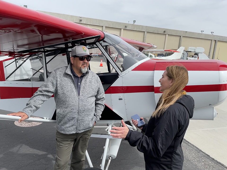 Director Sams and Kristin Swoboda stand next to a red and white airplane.