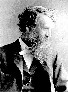 Black and white photo of John Muir in profile, wearing a suit, and sporting his trademark beard.