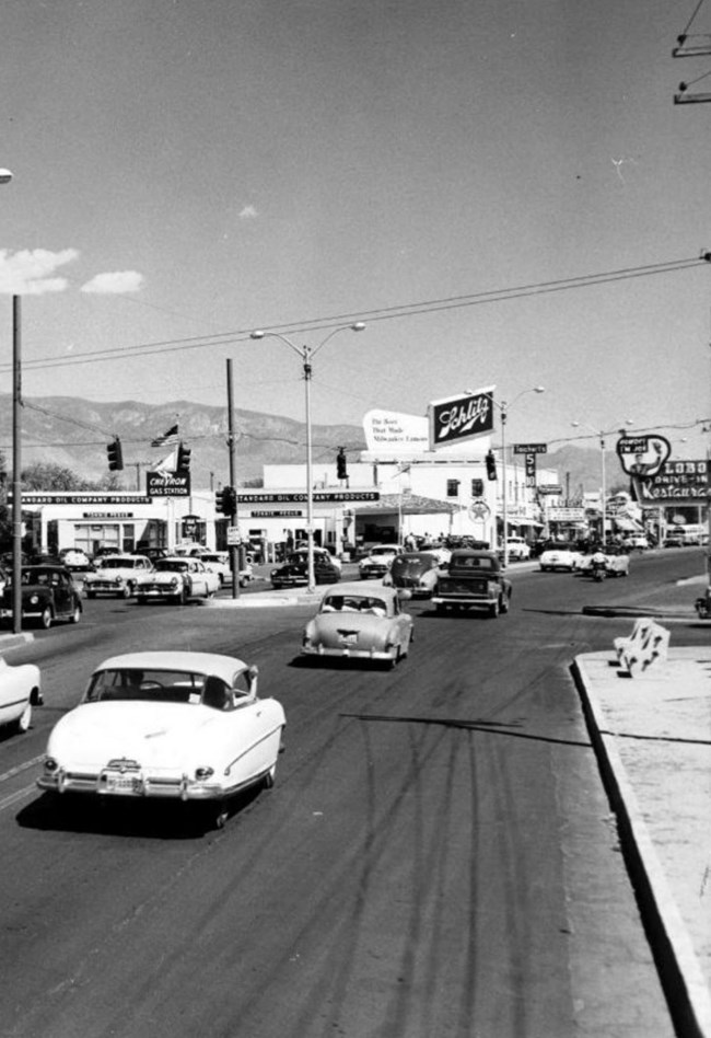 Historic image of 1960s era cars traveling on a road through a city.