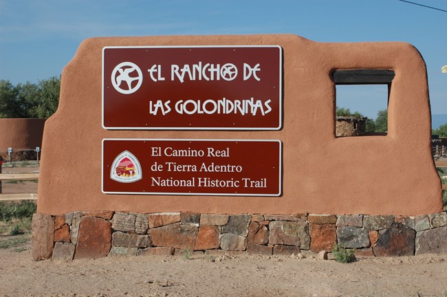 A large brown sign at the entrance to el Golondrinas, wrapped in adobe.