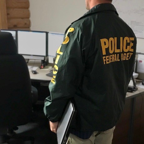 An ISB Special Agent stands near computer monitors, and carries a laptop computer under one arm. NPS photo.