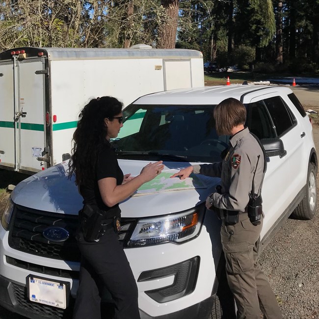 An ISB Special agent and US Park Ranger look at a map spread on the hood of a vehicle.