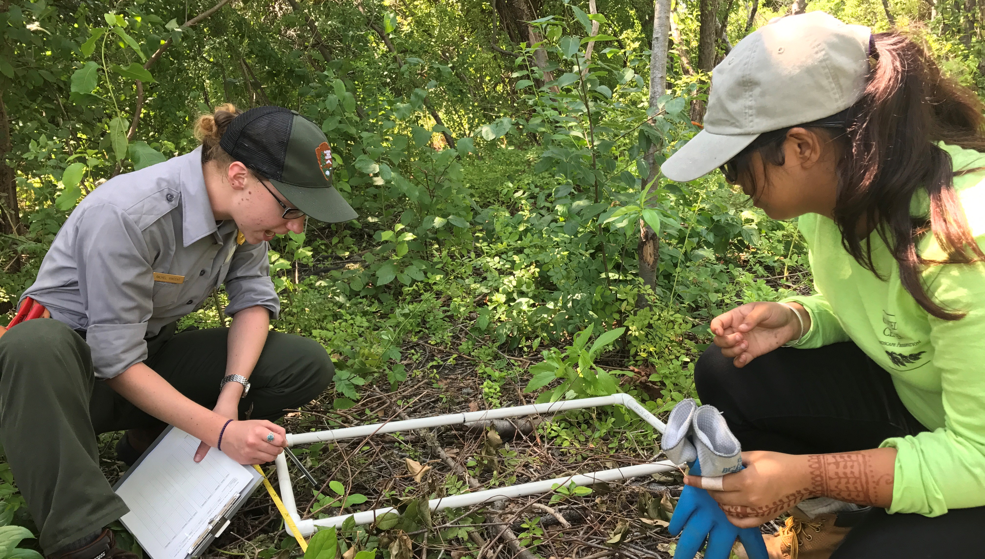 A person in NPS uniform with a clipboard points to the ground as a Branching Out participant looks on.
