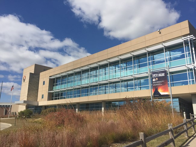 A tan long three story building with large windows.