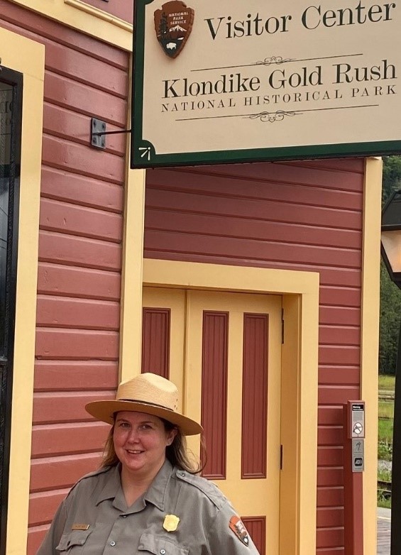 a park ranger standing near a sign that reads visitor center klondike gold rush national historical park