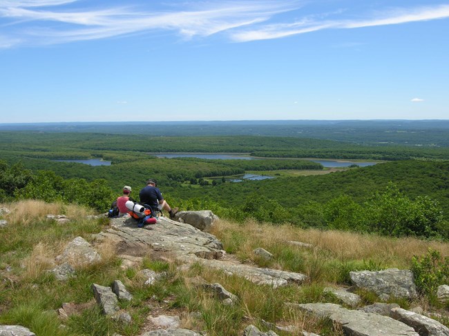 Two hikers rest overlooking a river.