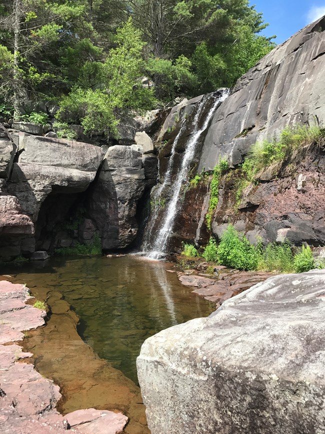 A waterfall flows down a cliff face into a clear pool near the Mongaup Falls hydroelectric project, New York, located on a tributary to the Upper Delaware Scenic and Recreational River.