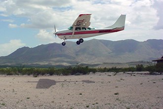 A patrol plane flies in for a landing in scrubby desert landscape.