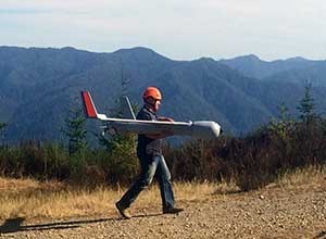 A man in a helmet carries an aircraft in his arms on a dirt trail.