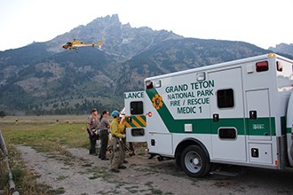 Rangers and crew members load a patient into an ambulance while a helicopter flies away.