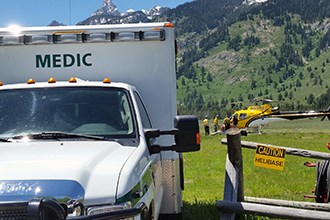 An ambulance waits at the entrance to a helibase while crew members unload a patient from a helicopter.