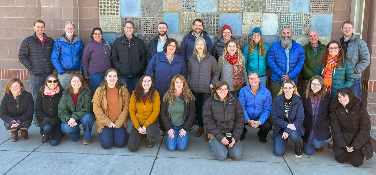 26 smiling people dressed in winter gear pose for a group photo