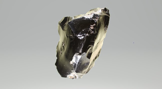 a piece of black obsidian with flakes chipped away, resulting in a shiny, swirled surface.
