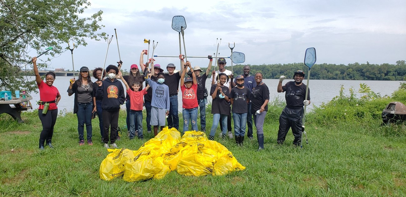A group of people holding trash pickers pose behind a line of full trash bags