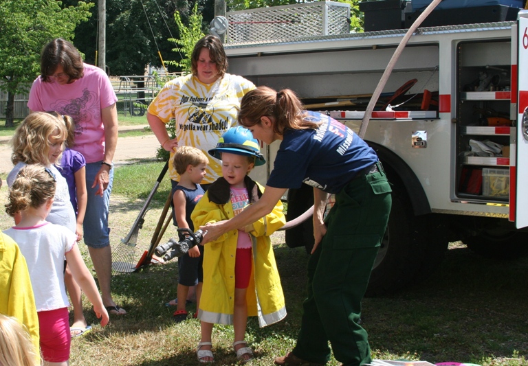 a group of kids, one dressed in firefighter uniform stand in front of a fire truck with nps staff for fire program.