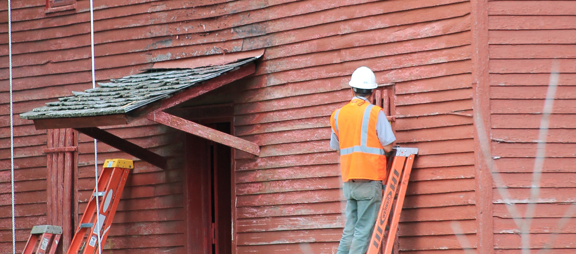 A man uses a paint scraper on an old red mill.