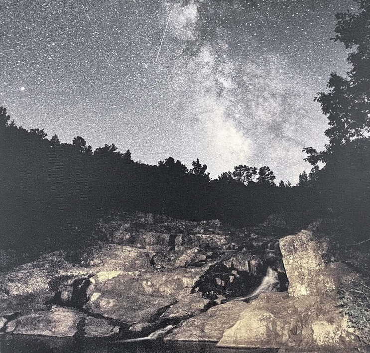 A nighttime picture of the rocks, sky and cascading water. The milky way is clearly visible in the sky with a shooting star.
