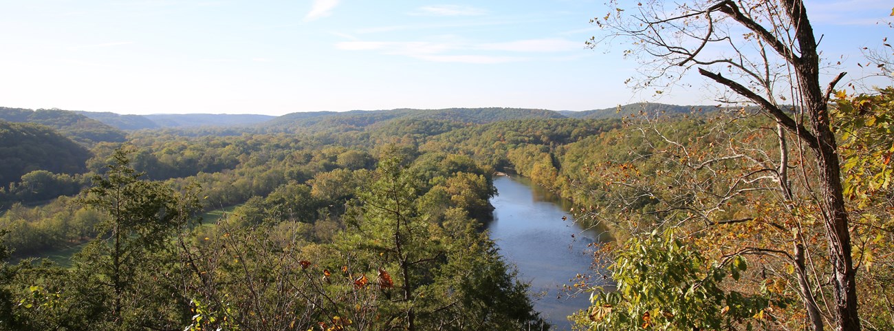 A panoramic view over Ozark mountains. A large river spans in the foreground, with fall colors on all sides.