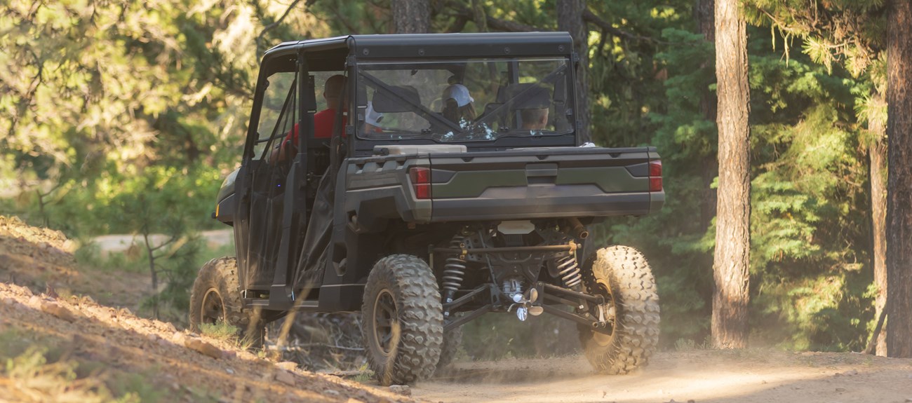 A side-by-side UTV drives down a dirt and gravel road.